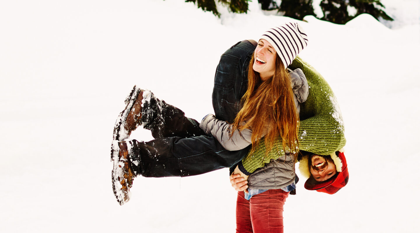 Eine Frau trägt ihren Freund auf der Schulter durch den Schnee.