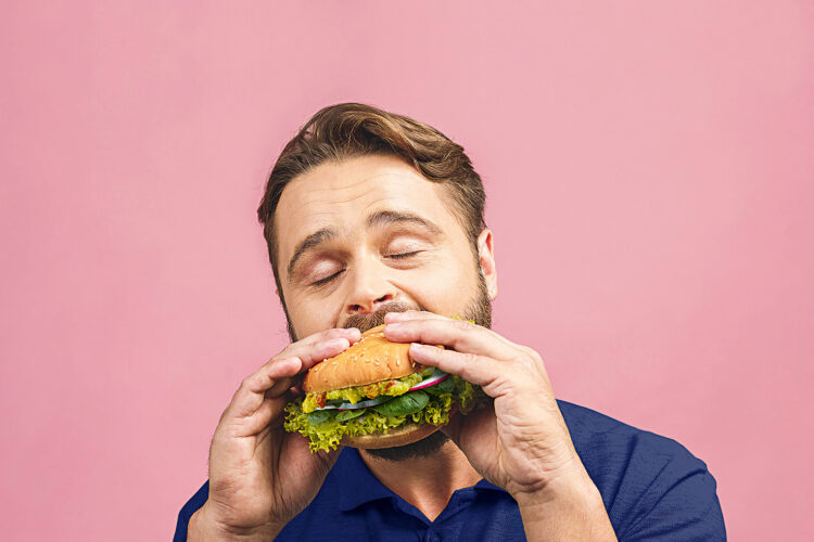 Ein Mann beißt genüsslich in einen Burger, der ausschließlich mit Gemüse belegt ist.